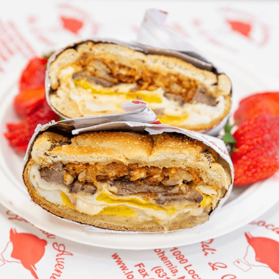 Two halves of a hearty deli sandwich with steak, eggs, and cheese, served with strawberries.