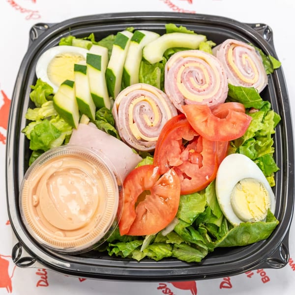 A deli salad with ham and cheese roll-ups, sliced cucumbers, tomatoes, and hard-boiled eggs.