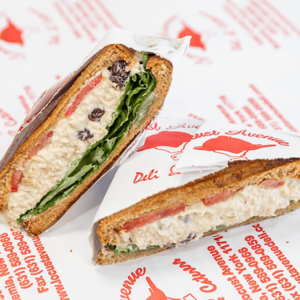 Two halves of a chicken salad sandwich with lettuce, tomato, and raisins on deli paper.