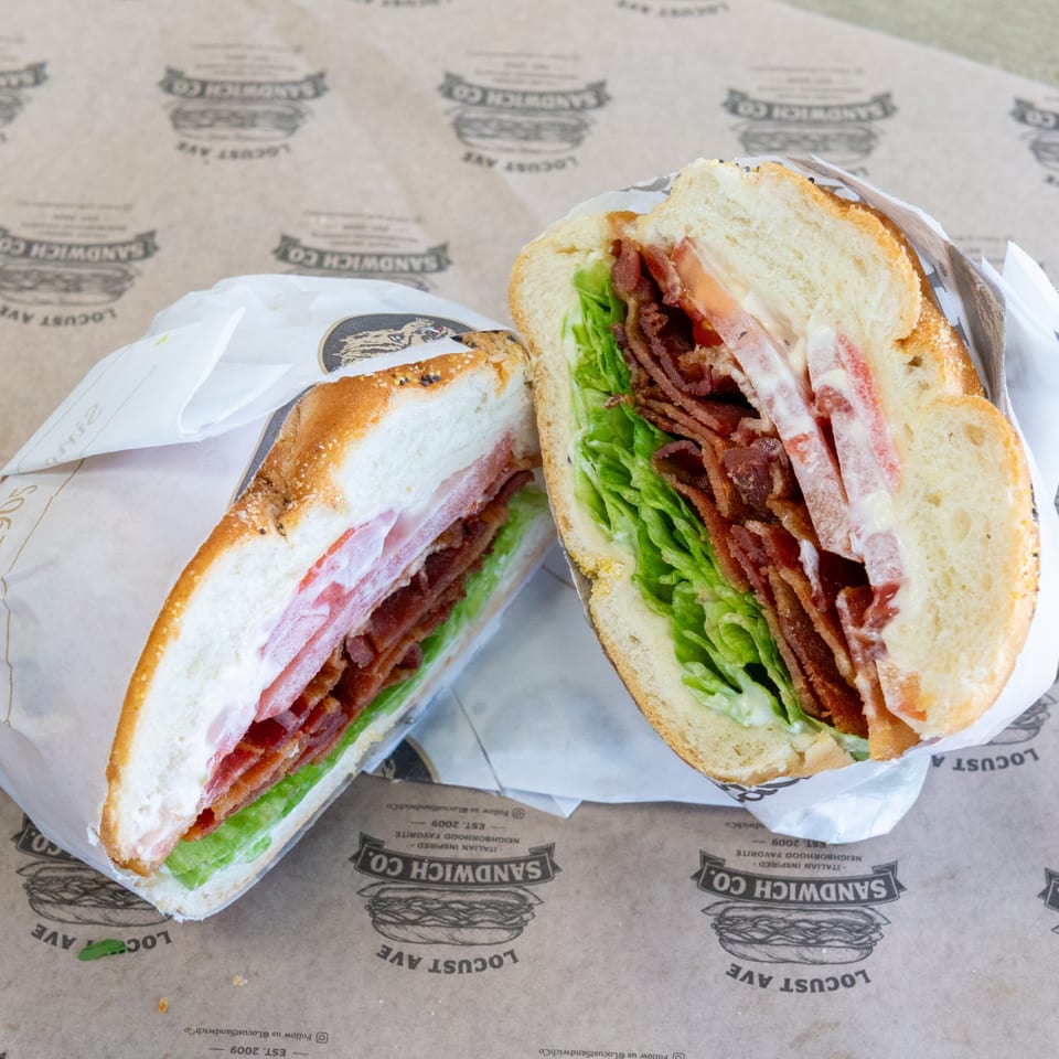 A BLT sandwich, cut in half, with bacon, lettuce, tomato, and mayonnaise on a roll.