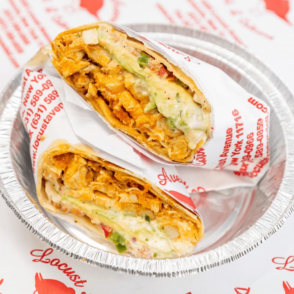 Two deli wraps, filled with chicken, cheese, and avocado, in a foil container.